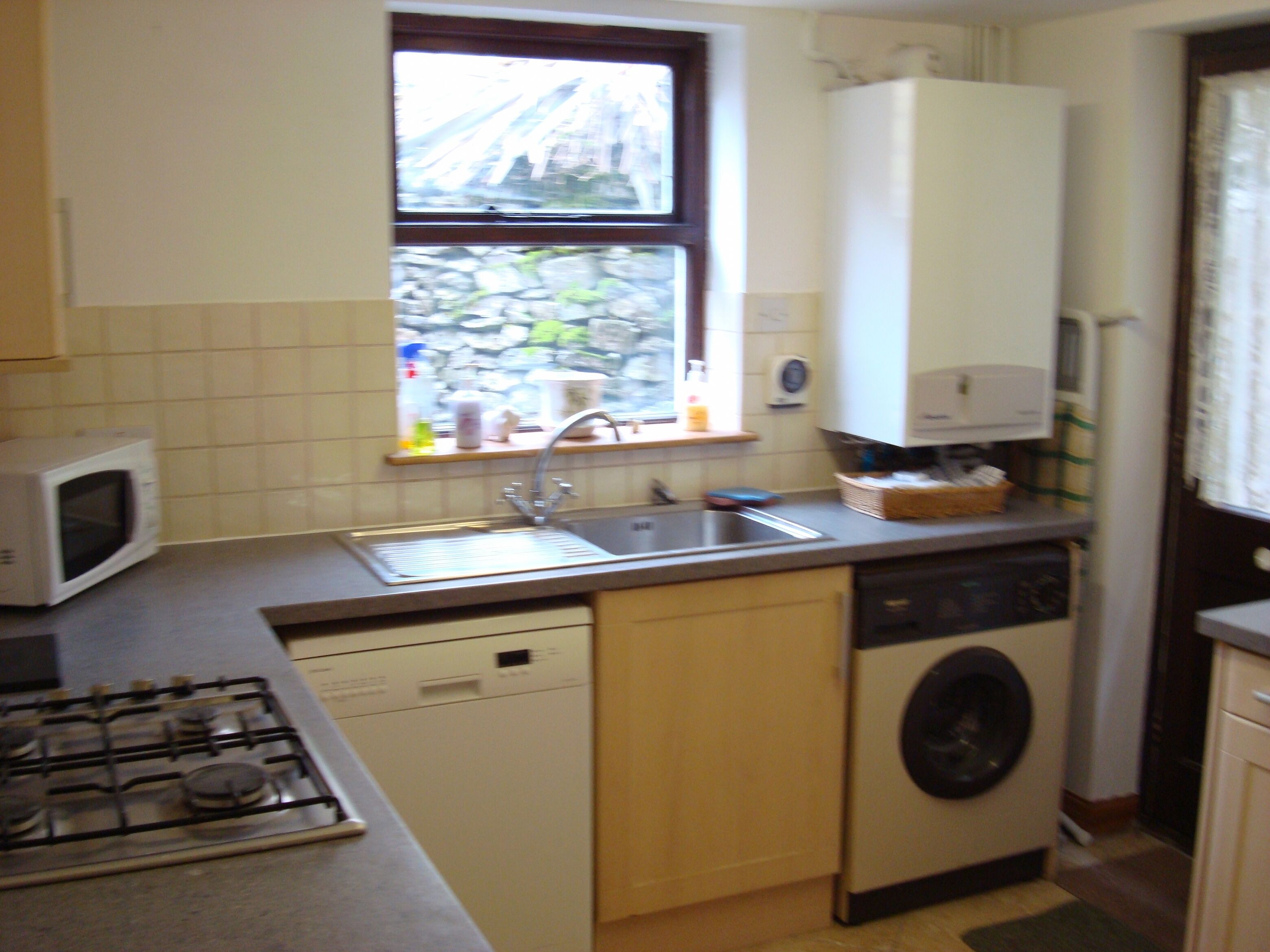 Een compacte keuken met een magnetron, spoelbak, fornuis en wasmachine.