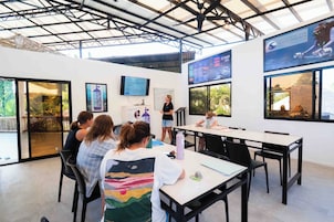 Un salón de conferencias con una pantalla de presentación, una pizarra y un grupo de personas sentadas en una mesa.