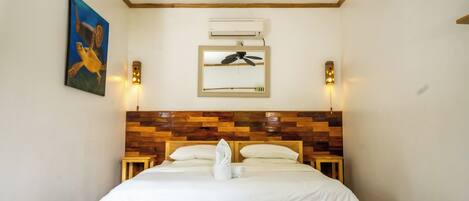 Habitación de hotel con cabecera de madera, cama con ropa de cama blanca, ventilador de techo y un cuadro en la pared.
