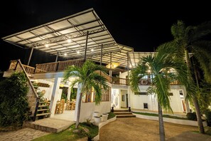 A two-story building with a covered outdoor seating area, palm trees, and a staircase leading to the upper level. - Liquid Dive Resort (Dauin)