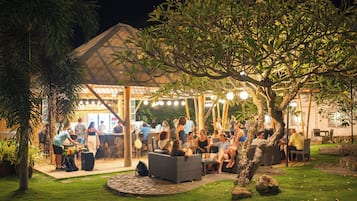 An outdoor dining area with tables and chairs, surrounded by greenery and a covered seating area.