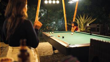 An outdoor pool table with a green felt surface, surrounded by a stone patio.