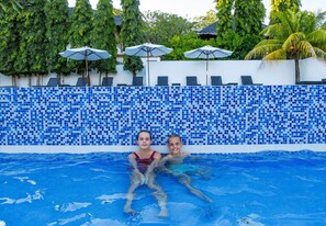 Una piscina con mosaicos azules, sillas de descanso y sombrillas.