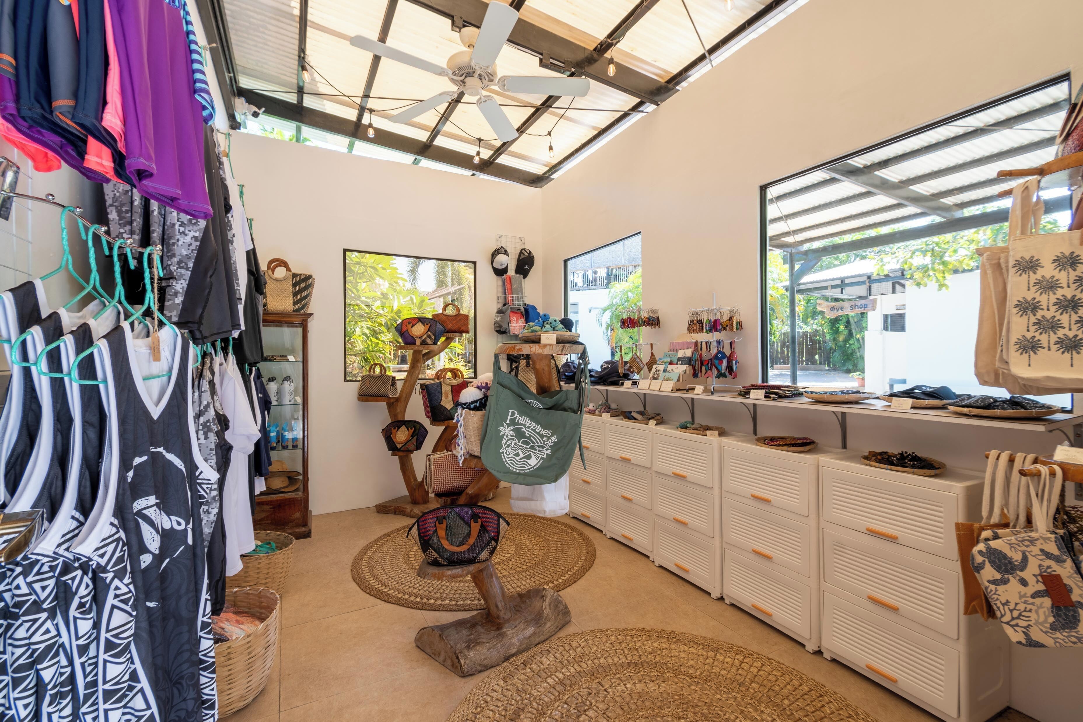 A boutique with clothing racks, a display of bags, and a ceiling fan.