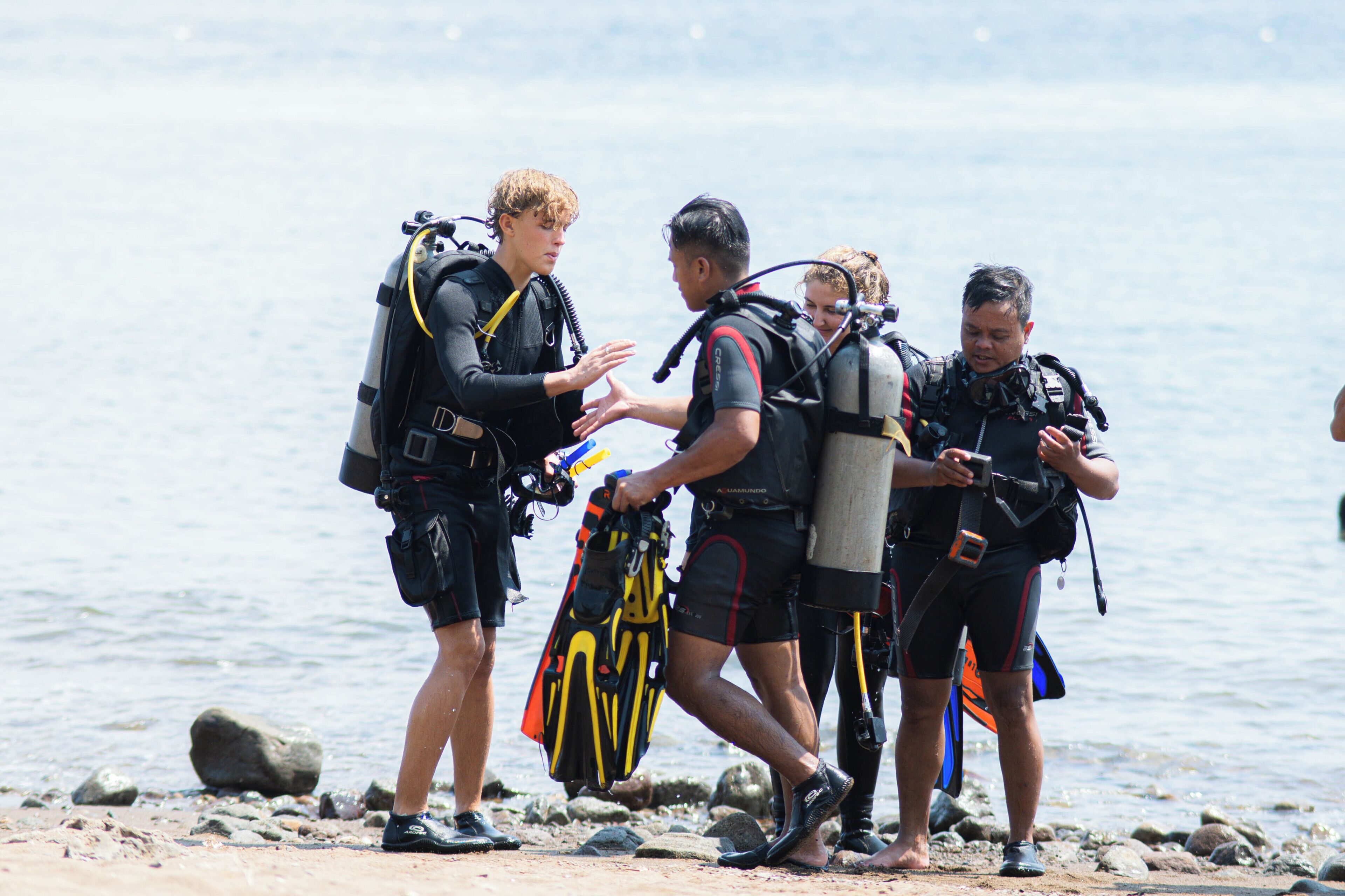 A group of divers on a rocky shore with water in the background.