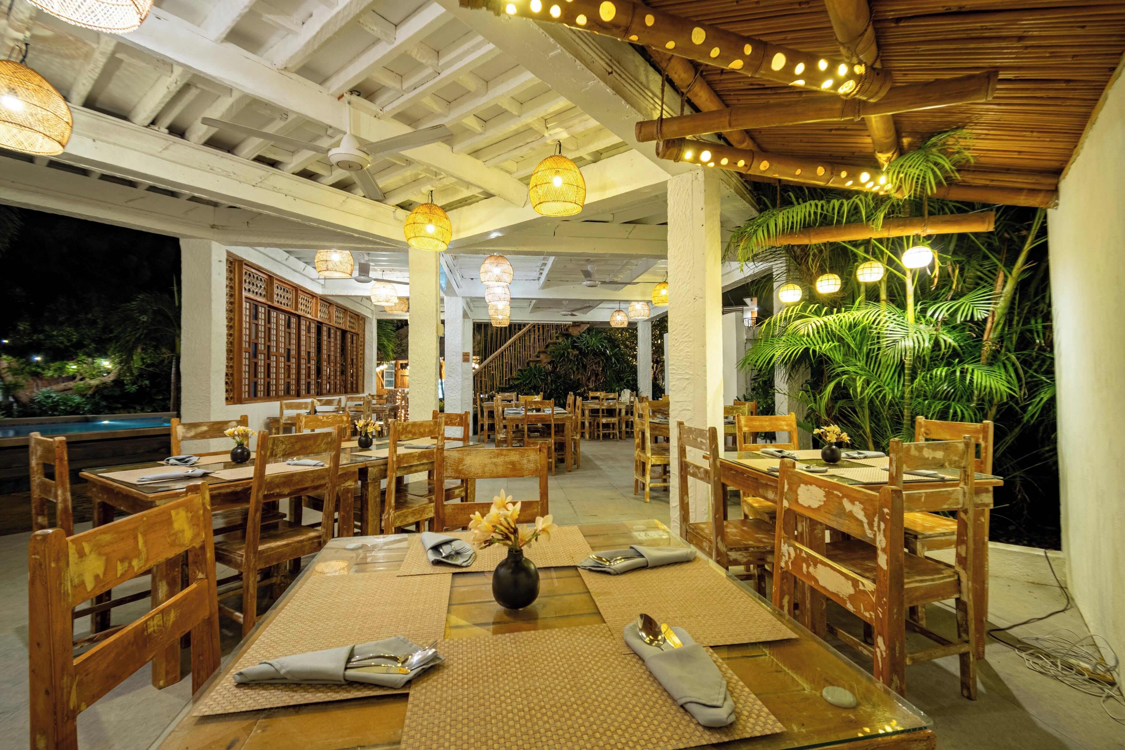 An indoor dining area with wooden tables and chairs, a central staircase, and hanging lights.