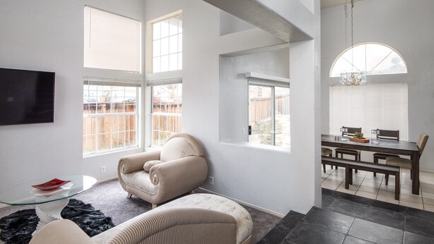A spacious living area with a modern design, featuring a glass coffee table, a beige sofa, and a dining area with a dark wooden table and chairs. - Hill View Home of the High Desert Victorville CA (Victorville)