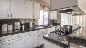 A kitchen with white cabinets, a granite countertop, a built-in stove, and a window with blinds. - Hill View Home of the High Desert Victorville CA (Victorville)
