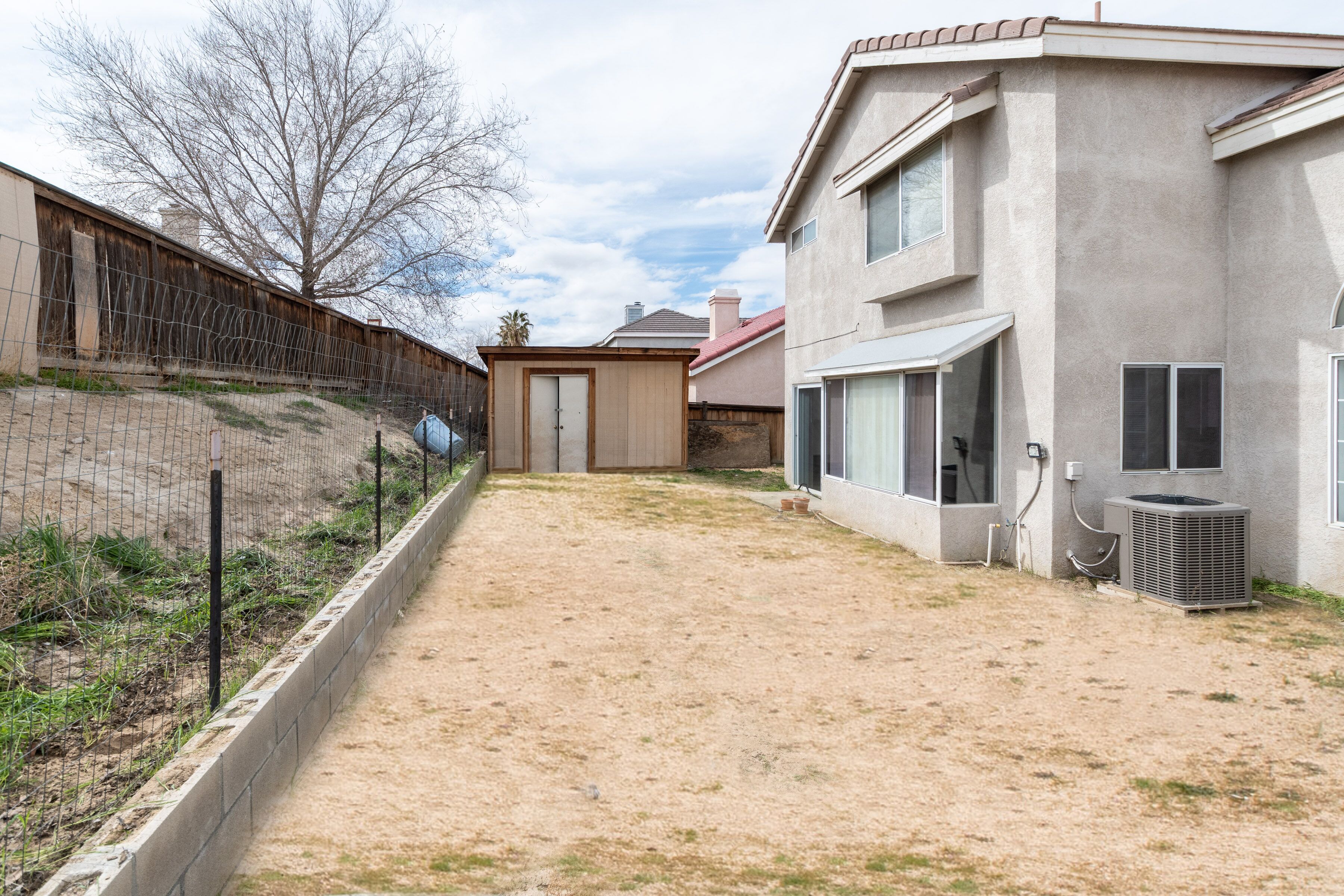 A residential area with a fenced yard, a small shed, and a two-story house with an air conditioning unit.