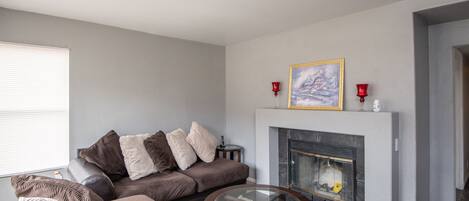 A living room with a sectional sofa, a glass coffee table, a fireplace, and a framed picture above the mantel.