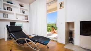 A room with a reclining chair, a TV, a fireplace, and a view of greenery outside.