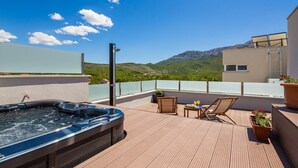 A rooftop terrace with a hot tub, wooden chairs, and a table with drinks.