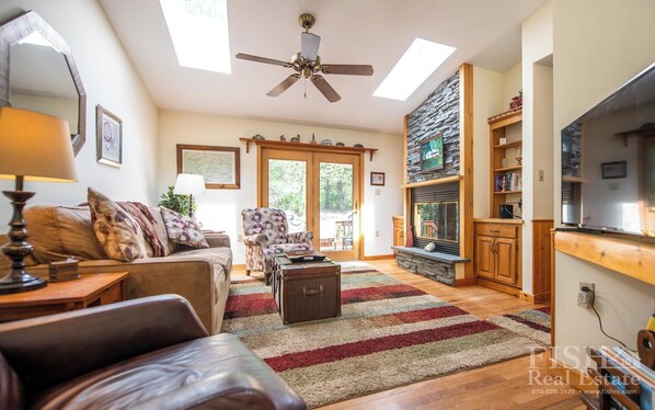 A spacious living room with a fireplace, wooden furniture, and a large window. - "Mulrooney's" is a ranch style home offering everything on the main level in Lake Mokoma (Laporte)