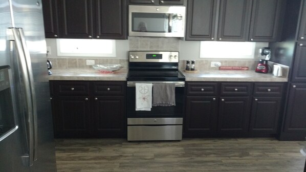 A kitchen with dark cabinets, a stainless steel refrigerator, a microwave, an oven, and a sink.
