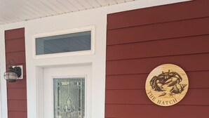Une porte d’entrée blanche avec un panneau de verre, une plaque en bois ornée d’un motif de crabe et une petite boîte aux lettres.