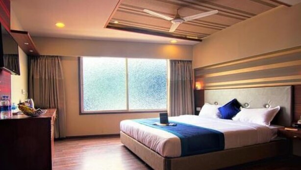 Habitación de hotel con una cama grande, un escritorio, una silla, una computadora portátil y una ventana con cortinas.