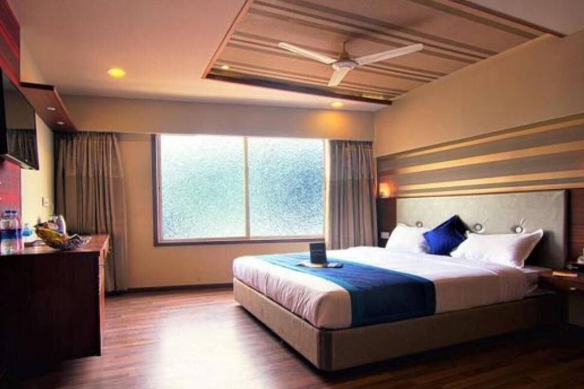 A hotel room with a bed, a desk, a chair, a window, and a ceiling fan.