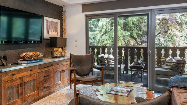 Un salon moderne doté d’un grand téléviseur, de meubles en bois, d’un coin salon confortable et d’un balcon aménagé avec du mobilier d’extérieur.