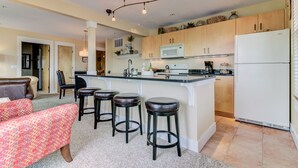 A modern kitchen with a central island, bar stools, and a refrigerator.