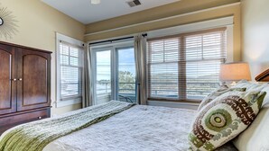 A bedroom with a large bed, a wooden wardrobe, and a view through the windows.