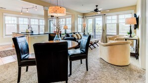 A spacious living room with a dining area, featuring a large chandelier, leather chairs, and a ceiling fan.