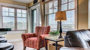 A living room with a patterned armchair, a leather sofa, a table with a lamp, and a view of the lake through large windows.