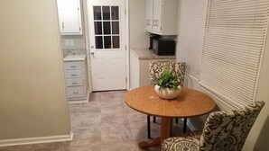 A compact kitchen with white cabinets, a white door, and a round wooden table with a potted plant. - Great location! 5 min. to Downtown, Medical District, and the Masters. (Augusta)