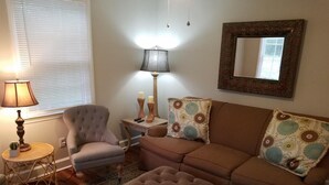 A living room with a sofa, armchair, ottoman, lamp, and a mirror on the wall. - Great location! 5 min. to Downtown, Medical District, and the Masters. (Augusta)