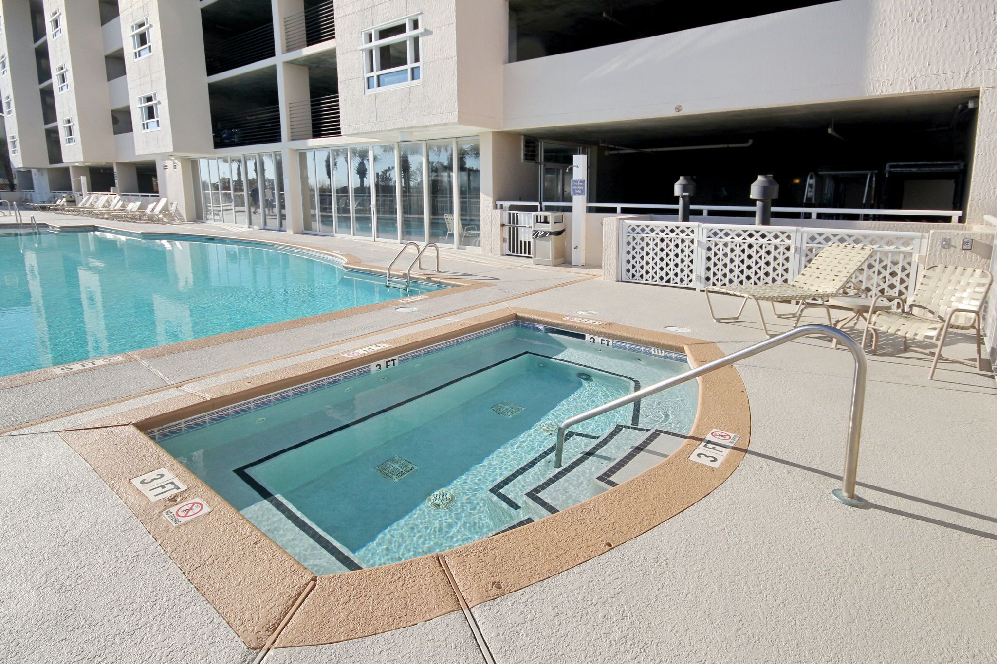 A pool area with two pools, lounge chairs, and a covered seating area.