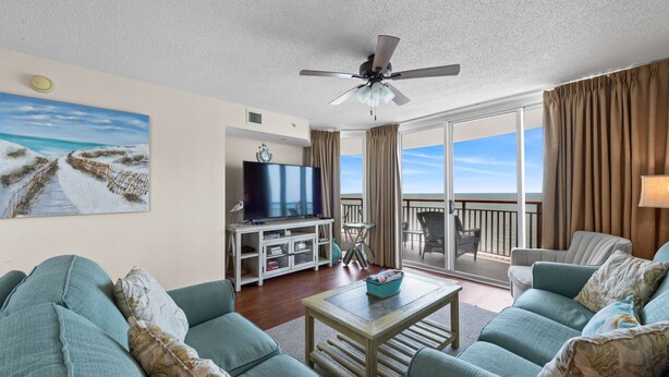 A living room with a TV, sofa, and a balcony with a view.
