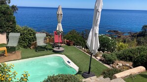 Ein Poolbereich mit Blick auf das Meer, umgeben von Grünpflanzen und Gartenmöbeln.