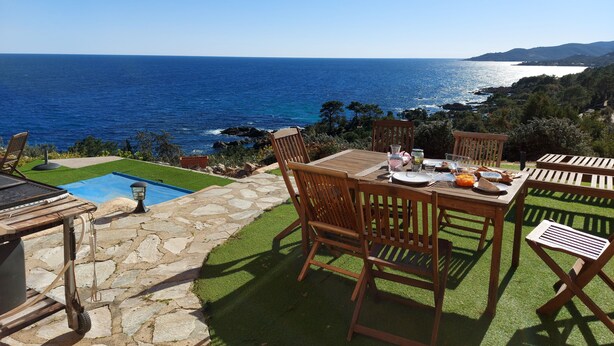 Eine Terrasse mit Esstisch, mit Blick auf die Küste, das Meer und die Hügel.
