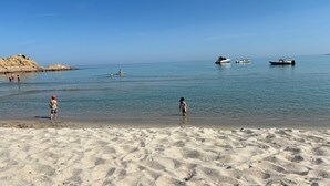 Ein Sandstrand mit klarem Wasser, Booten und Menschen.