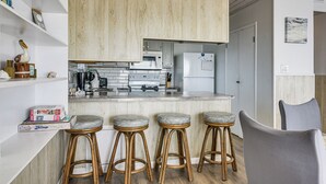 A modern kitchen with wooden cabinets, a marble countertop, and three bar stools. - Beachfront Serenity in Galveston! Group-Ready Home (Galveston)
