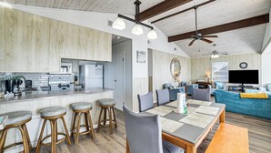 A modern kitchen with bar stools, a dining area with a table and chairs, and a living room with a sofa and TV. - Beachfront Serenity in Galveston! Group-Ready Home (Galveston)