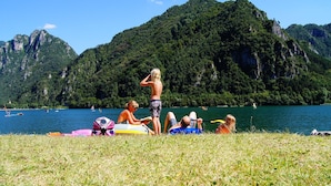 A group of people relaxing on a grassy area with a lake and mountains in the background. - Directly on the lake with terrace (Tre Capitelli)