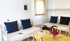Una stanza con due letti singoli, un tavolo in legno con un vaso di fiori e un quadro appeso al muro.