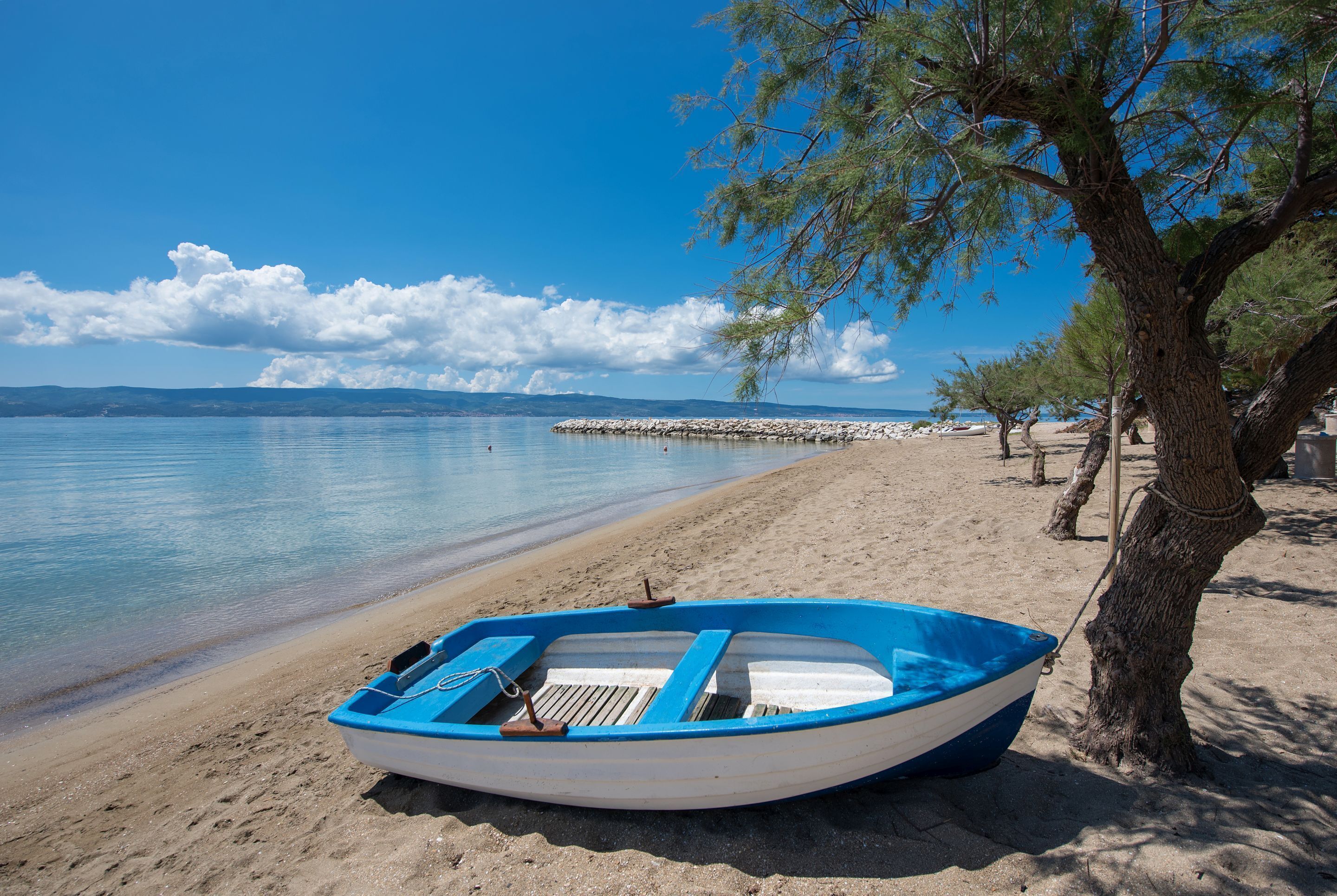 A small blue boat on a sandy beach with a clear blue sky and calm water.