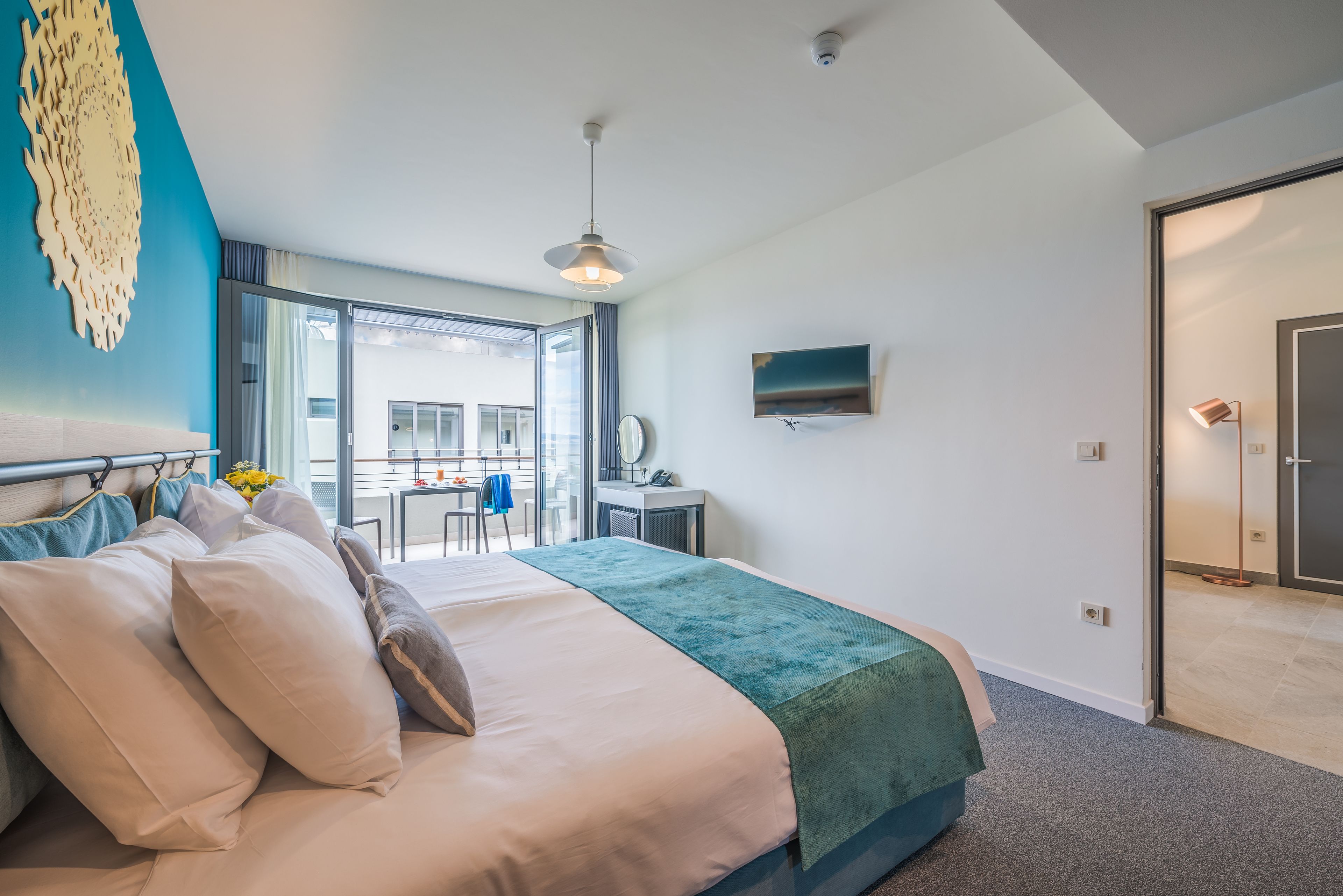 Una habitación de hotel moderna con una cama grande, un escritorio, un televisor y un balcón con vistas.