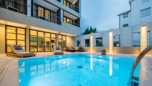 A modern outdoor swimming pool with lounge chairs and a glass-enclosed patio area. - Hotel Nestos (Dugi Rat)