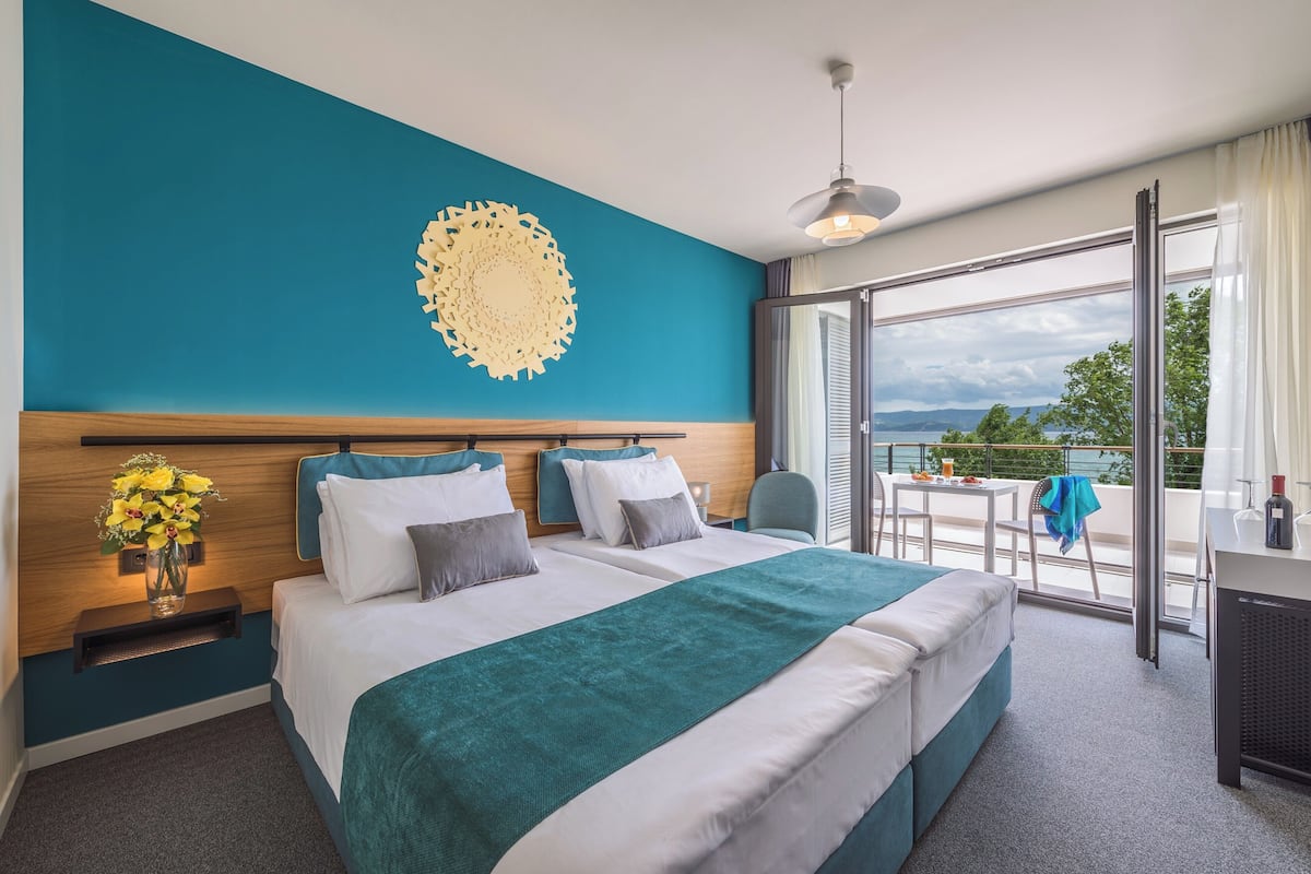 Habitación de hotel con una cama grande, un escritorio, una silla, un balcón con vistas y un adorno decorativo en la pared.