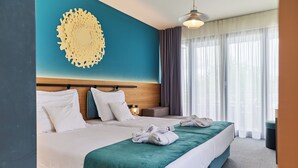 A hotel room with a large bed, a headboard, a wall decoration, a bedside table, a lamp, a window with curtains, and a trash bin. - Hotel Nestos (Dugi Rat)