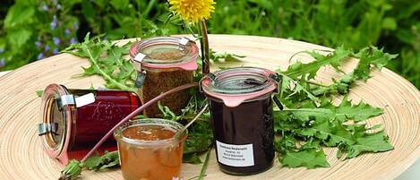 A wooden tray with jars of honey and a honey dipper, surrounded by green leaves and a yellow flower.