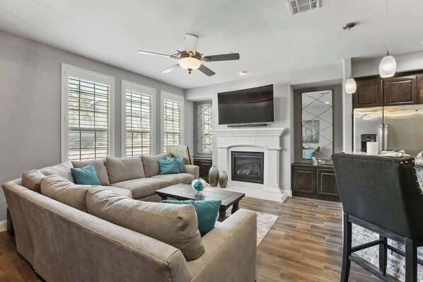 A modern living room with a sectional sofa, a fireplace, a television, and a dining area.