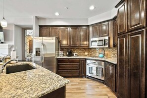 A kitchen with dark wood cabinets, a granite countertop, stainless steel appliances, and a tiled backsplash.