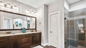 Une salle de bain dotée d’un grand miroir, d’un meuble-lavabo en bois foncé et d’un espace douche avec des portes en verre.
