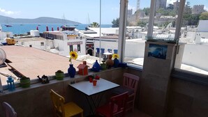 A terrace with a table and chairs, potted plants, and a view of the sea and buildings. - Can Hotel (Bodrum)