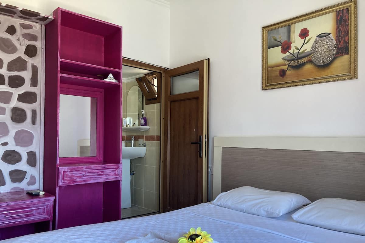 Habitación de hotel con cama, un armario rosa, baño con espejo y un cuadro en la pared.