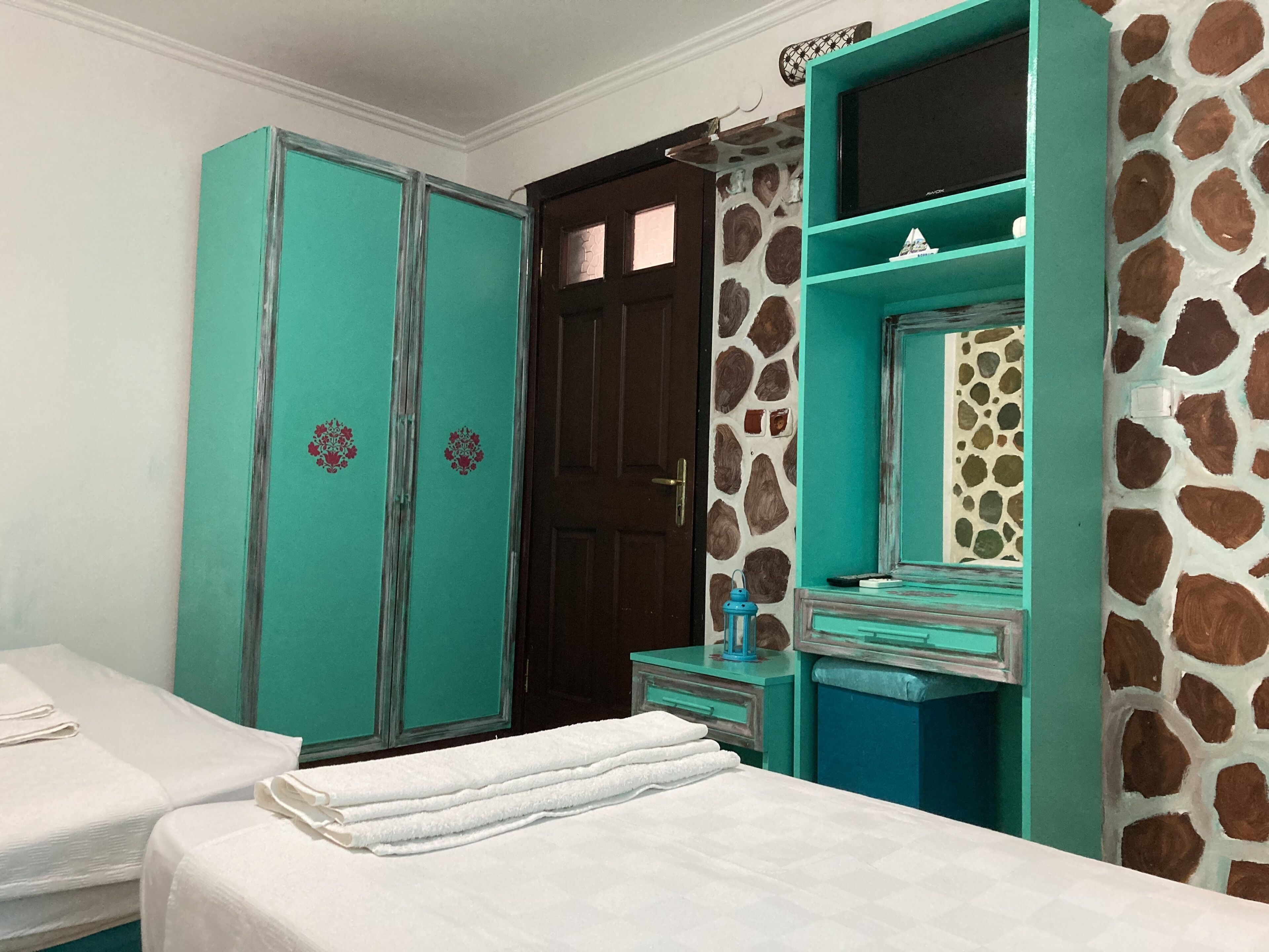 A room with teal-colored wardrobes, a bed with white linens, and a bathroom with a mirror and a towel rack.