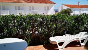 Een terras met een tafel en lounge stoelen, een tegelvloer en een haag.